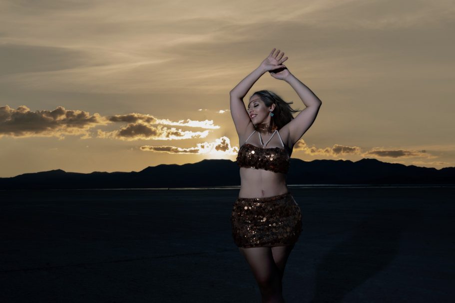A woman in a sparkling outfit dances against a sunset backdrop.