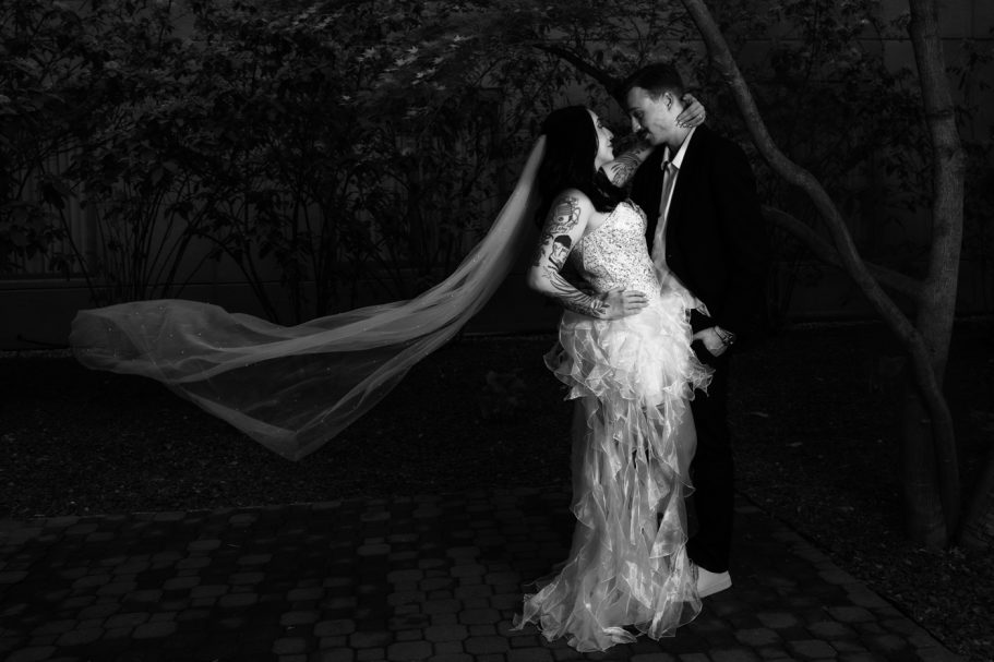Couple sharing a romantic kiss, dressed elegantly in wedding attire, surrounded by soft lighting.