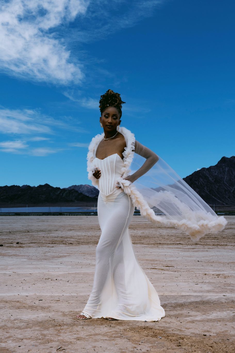 A model in a flowing white gown poses against a dramatic natural backdrop.