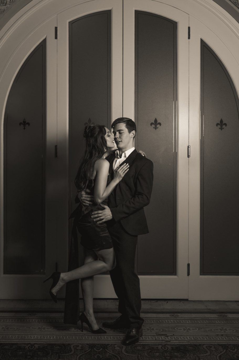 Couple in formal attire poses closely against a vintage-style door.