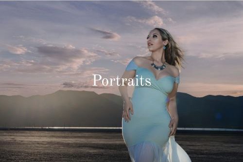 Photograph of a woman in a flowing light blue dress poses against a scenic sunset backdrop.