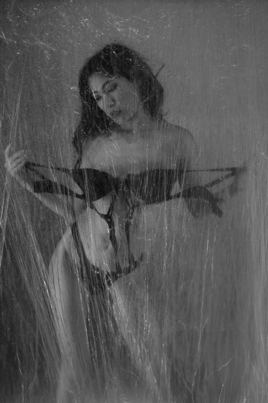 A figure gently holding lingerie, partially obscured by a translucent curtain.