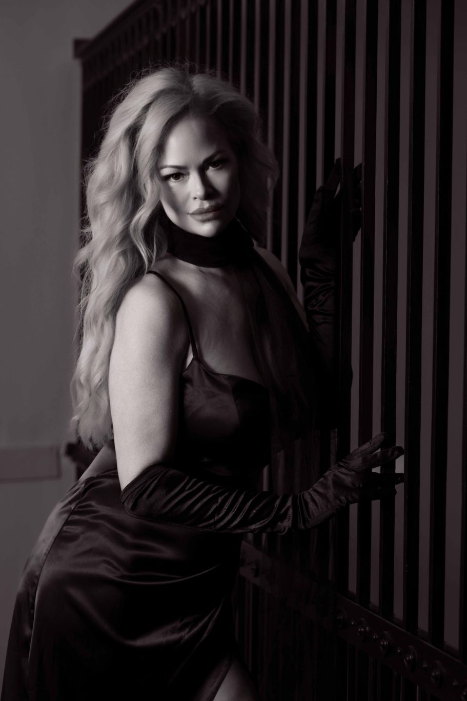 Woman in a black dress with long hair, posing near vertical striated surfaces.