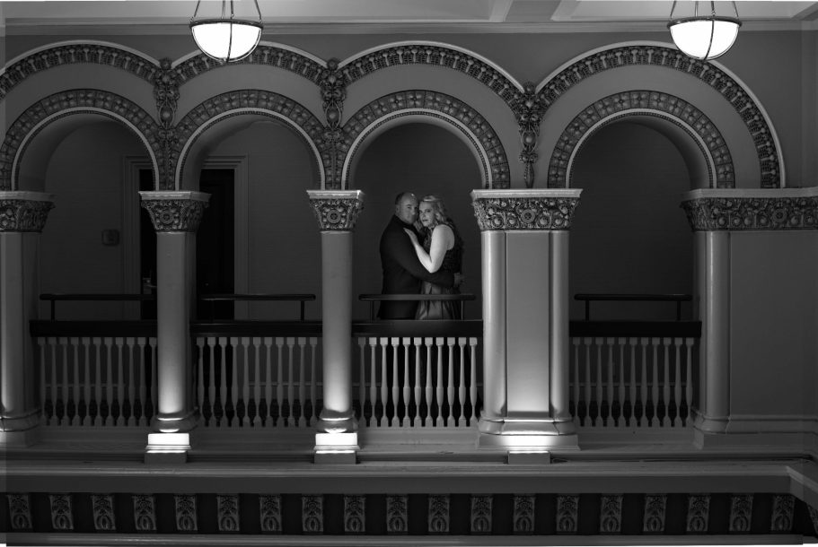 A couple embraces under ornate archways in a dimly lit corridor.