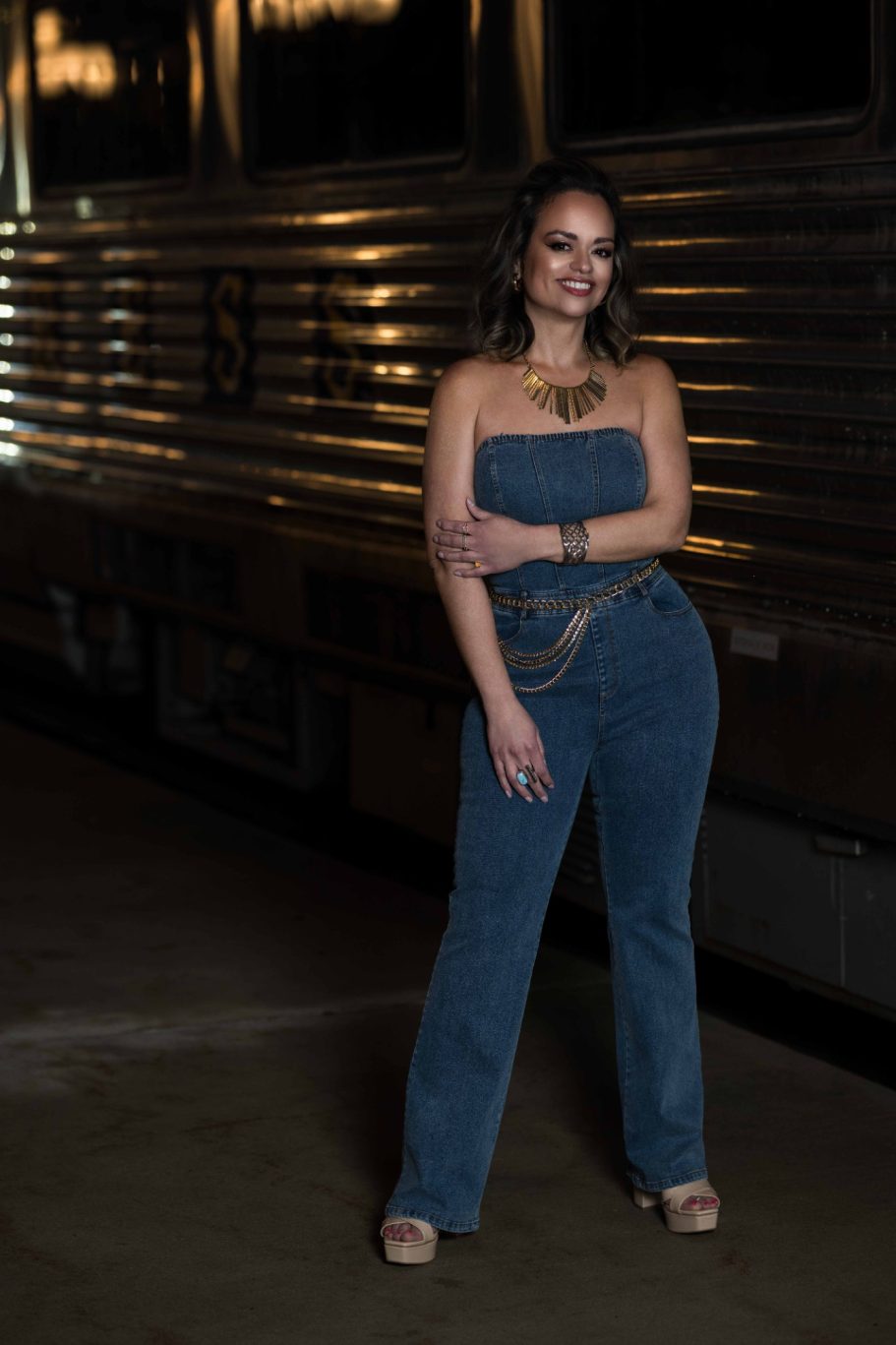 Woman in a strapless denim outfit poses confidently against a vintage train backdrop.